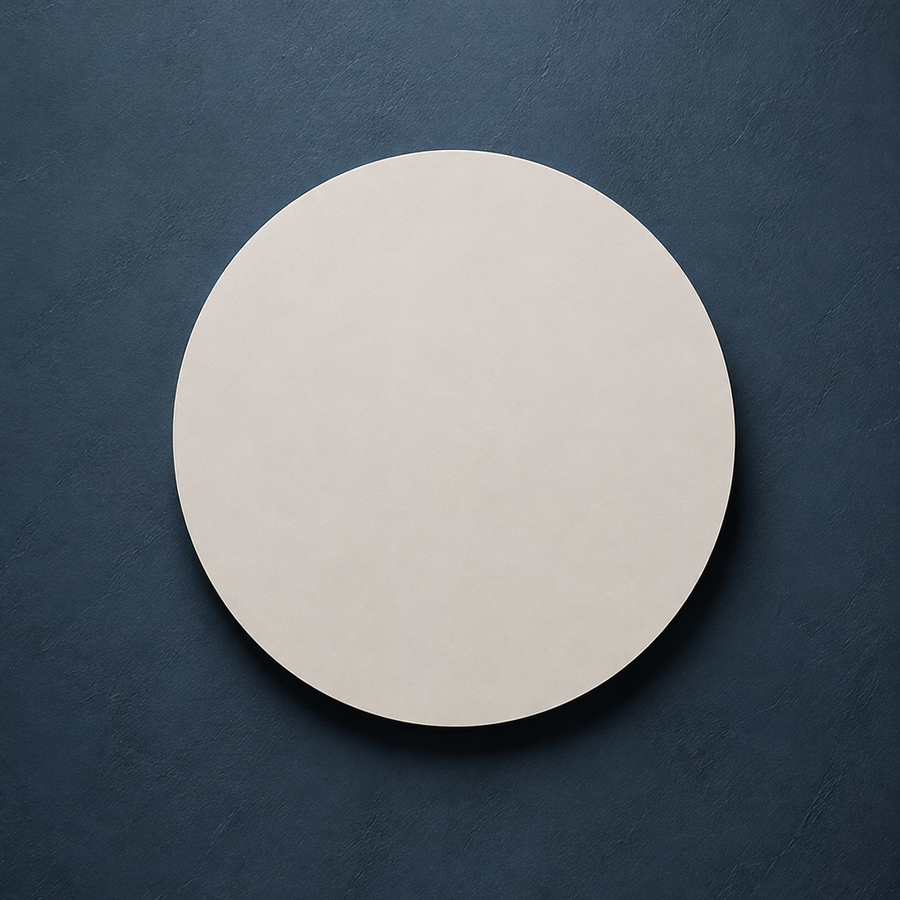 A minimalist, round off-white ceramic plate or tray centered on a dark textured slate background.